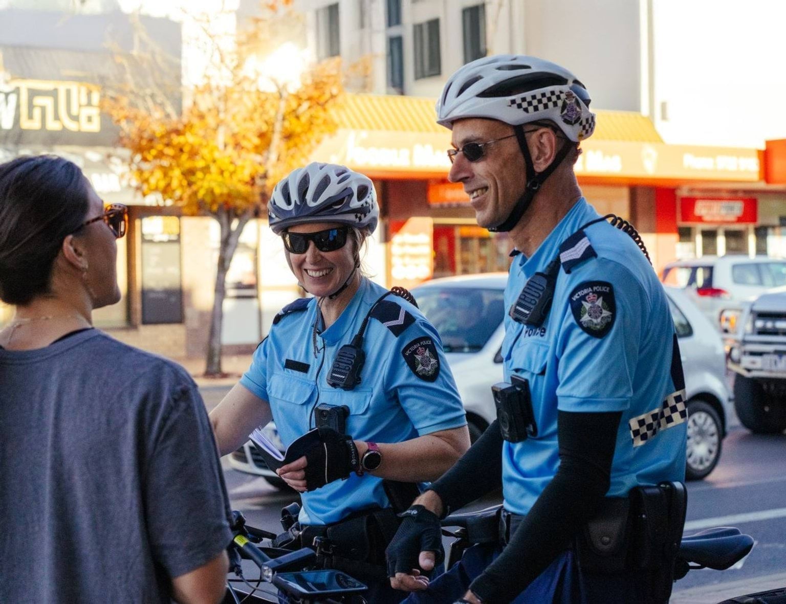 Two police officers on bicycles, talking to a member of the public.