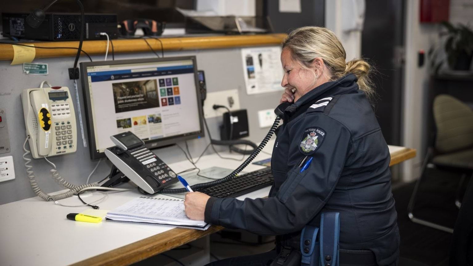 Female police officer taking a call at a desk.