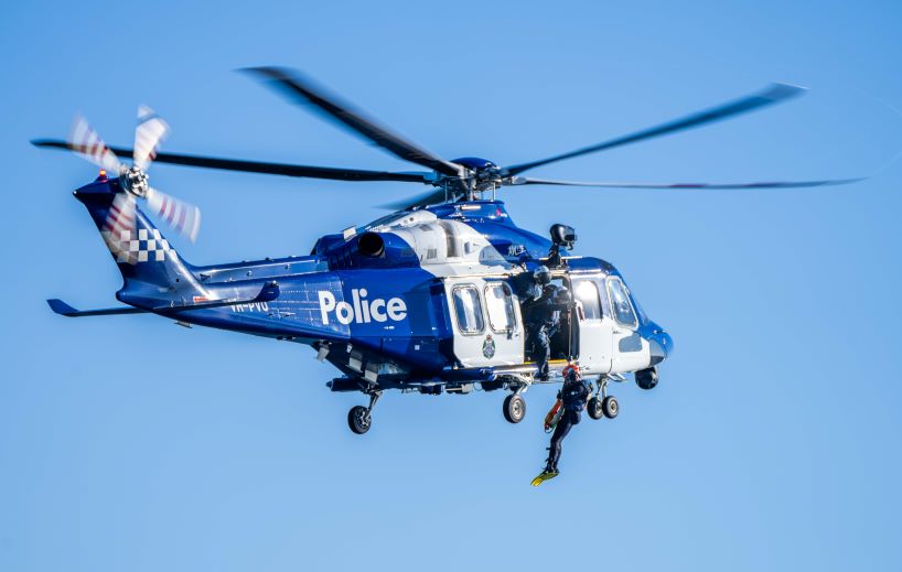 A Victoria Police member being winched out of a police helicopter over the water