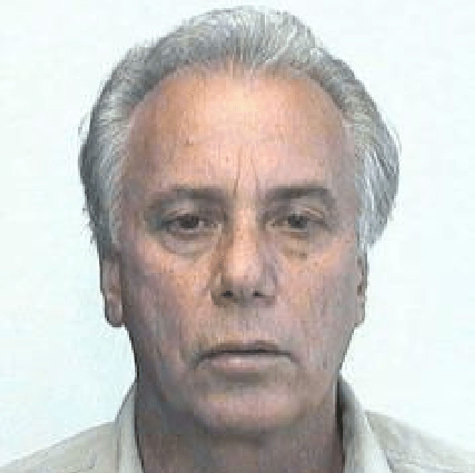A close-up photo of a 58-year-old man's face. He is of Greek descent with silver hair, and is staring directly at the camera. 