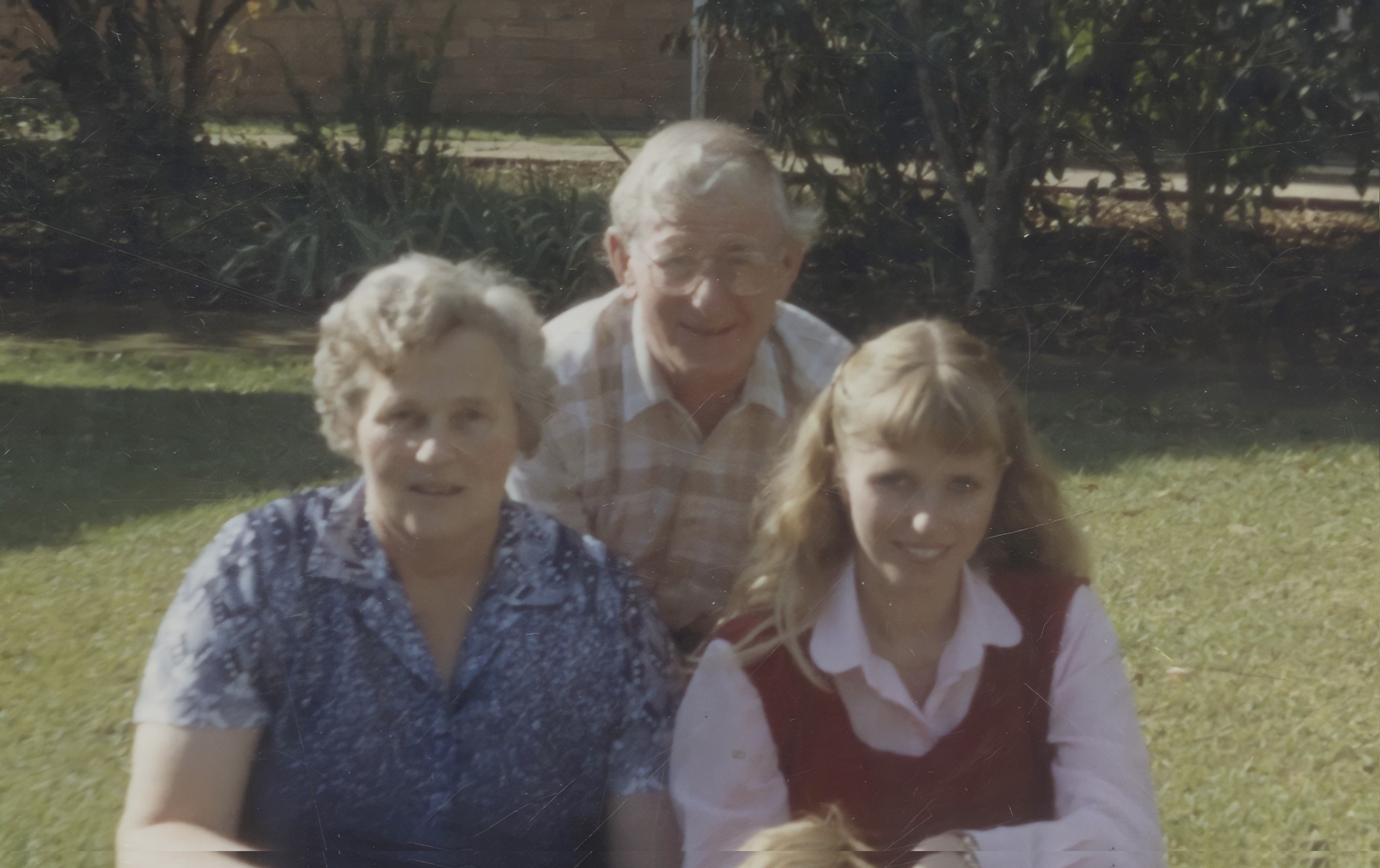 A 64-year-old white man is posing with his wife and another woman. His has silver white hair, a yellow and brown checked shirt and glasses. All three are happily smiling at the camera.