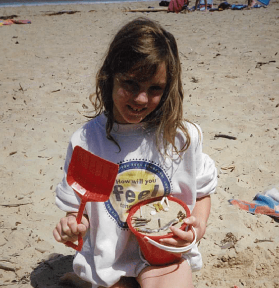 Cherie Westell at the beach with shoulder length dark brown hair, wearing a white jumper.