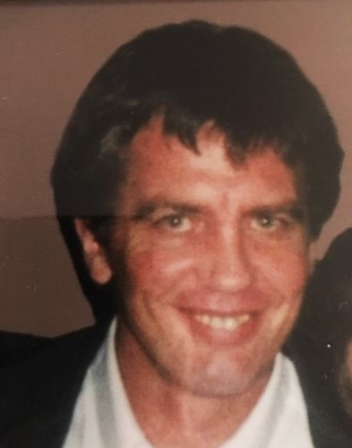 A photo of missing person Selman (Sam) Mala. The photo shows a man with medium length very dark brown or black hair, of Caucasian appearance. He is smiling and looking directly at the camera. He is wearing a white dress shirt and black dress jacket. The photo appears to be from the 1990s. He appears to be in his early or mid 30s.