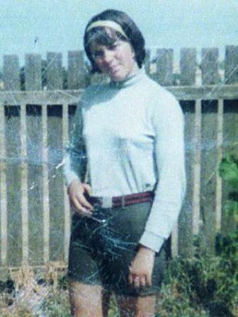 Maureen Braddy wearing a white long sleeve top, shorts and a red belt. Her hair is brown hair with a fringe, and wearing a white headband.