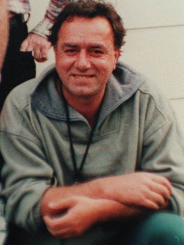 Gianni 'John' Furlan, smiling at the camera, with short brown hair, wearing a grey jumper and blue pants. 