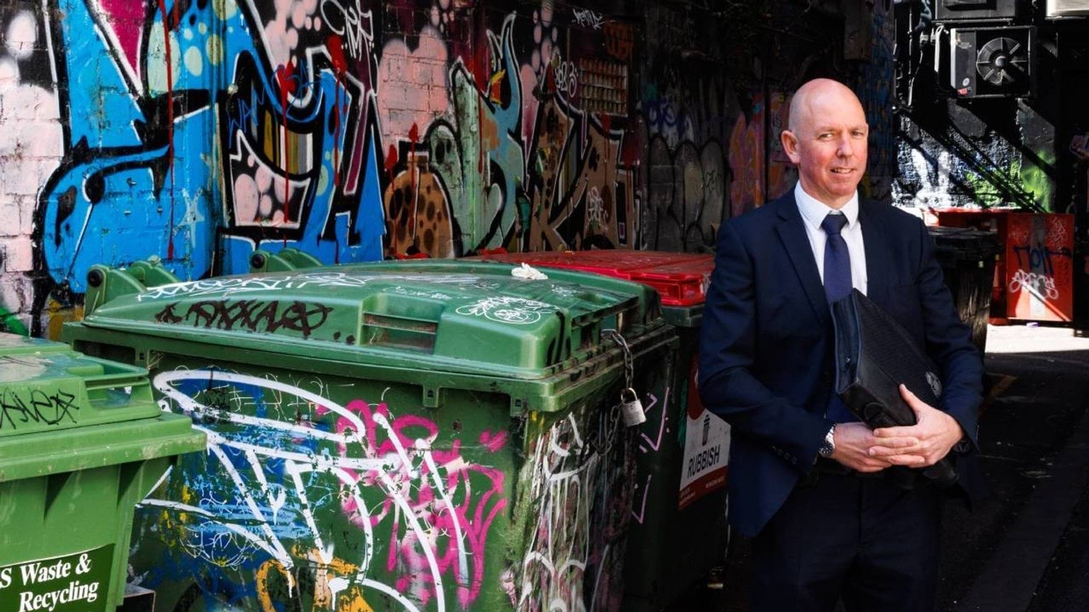 Police Life stories - Perseverance pays off - detective in front of graffiti wall and bins