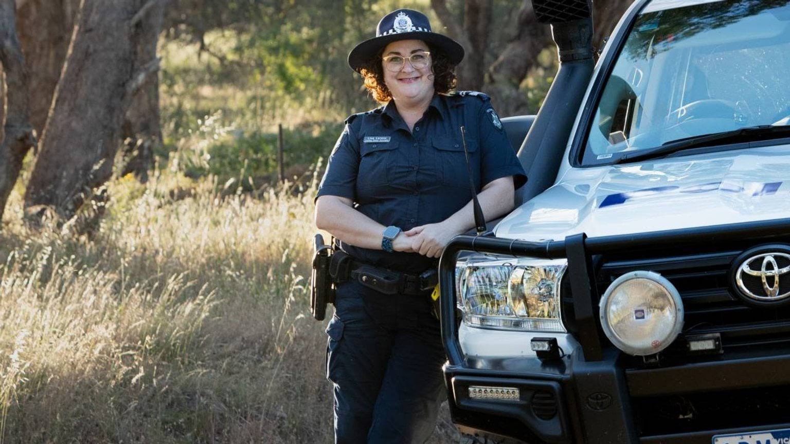 About us - Police Life stories - Bilingual officers - A female officer in the bush leaning on a police vehicle