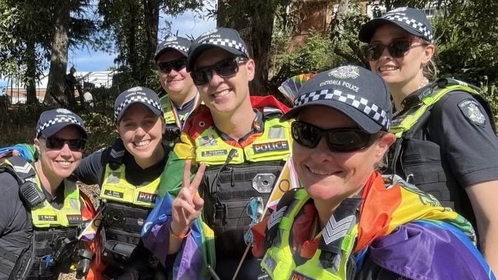 Police officers standing together with a rainbow coloured flag. 