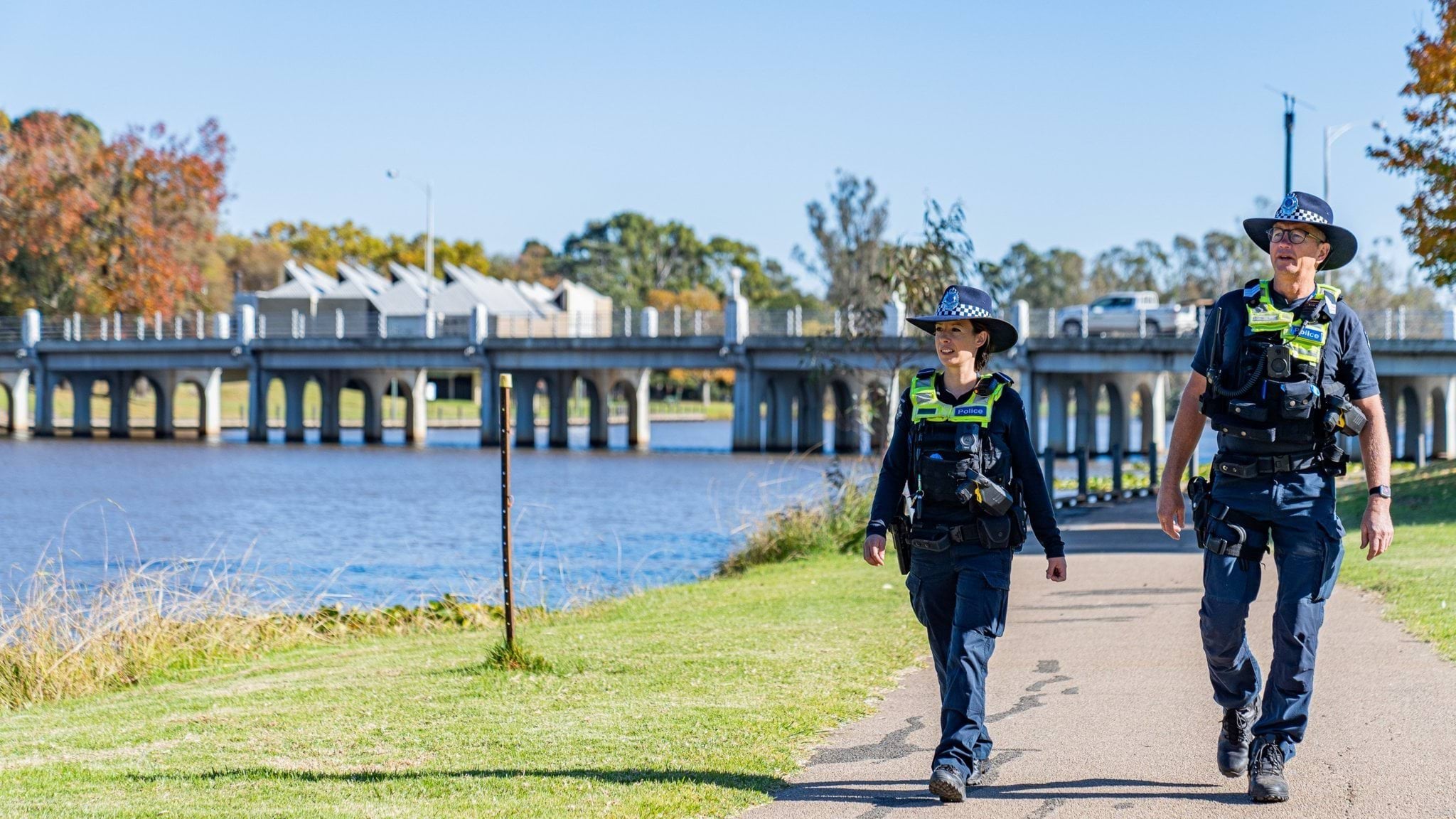 Two officers in police uniform walking on a footpath next to a river. 