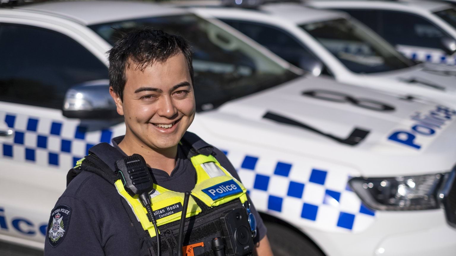 Police officer Constable Caillan Hoole with police cars in background.