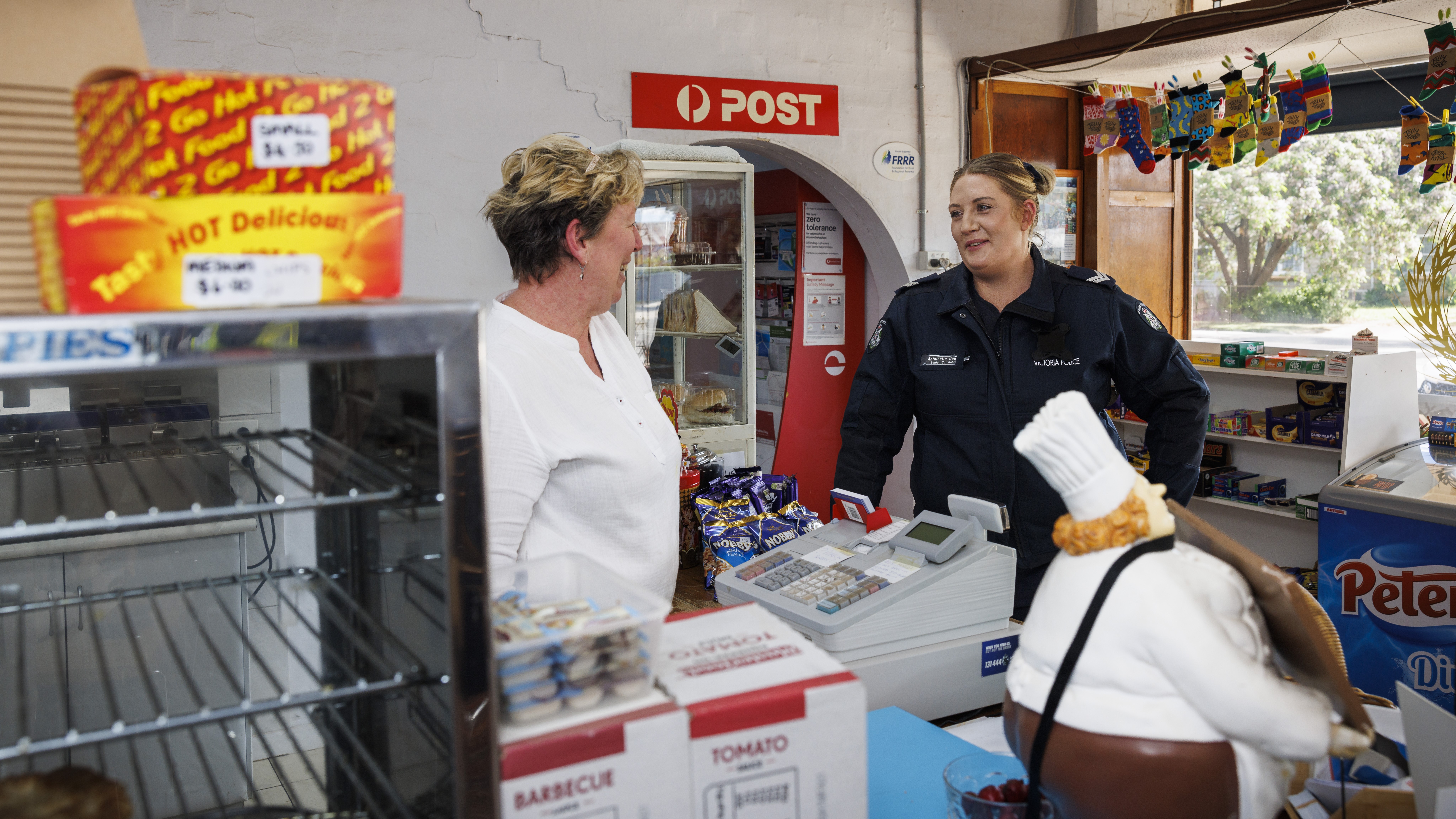 Police Life - Image of female behind the counter at a post office talking to female police officer who is in uniform.