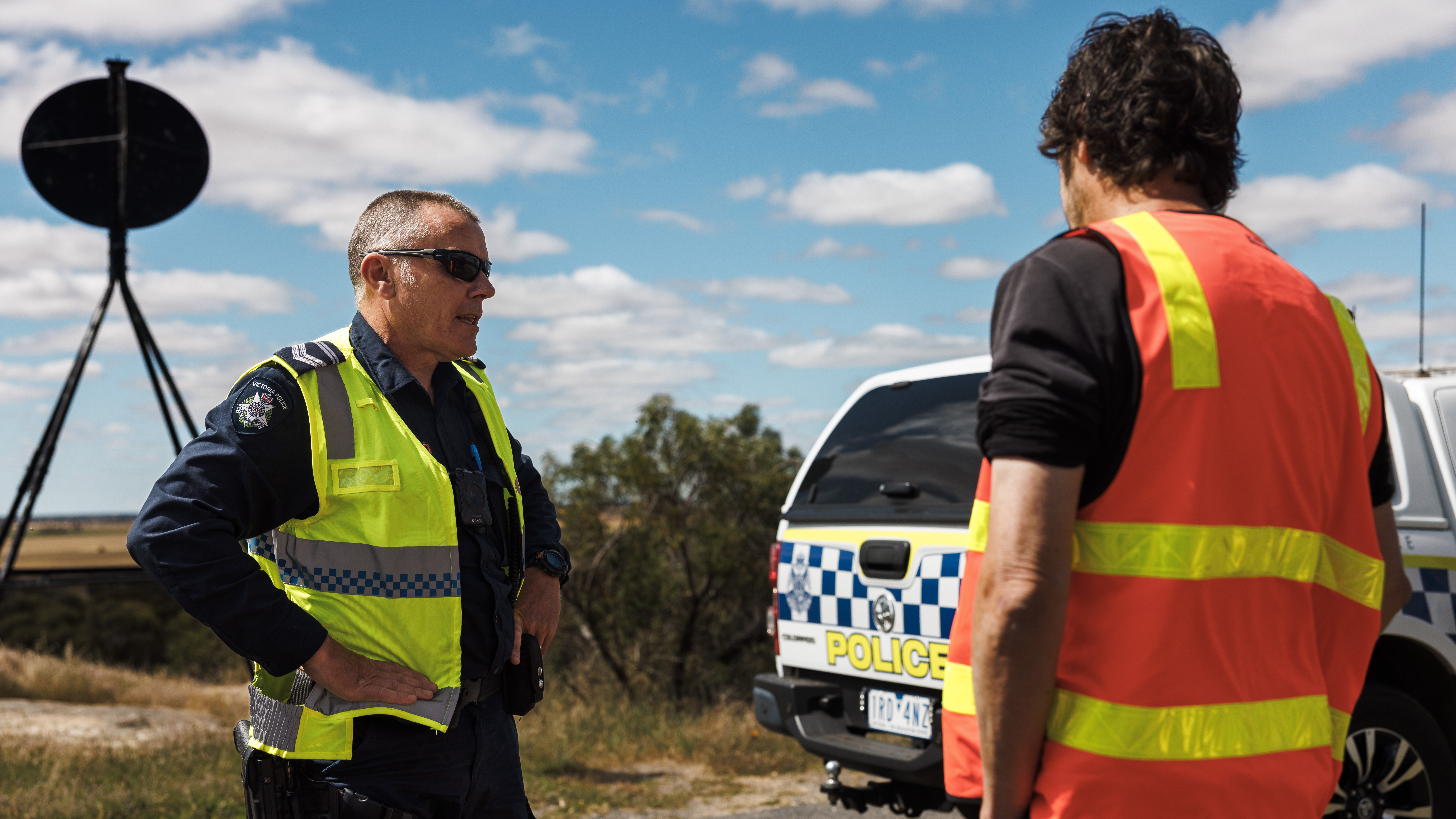 Police Life - image of male police officer wearing high-vis vest talking to another man in a high-vis vest. 