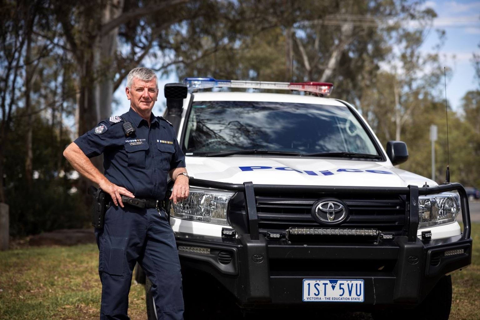 Senior Sergeant Wayne Spence standing beside a police vehicle.