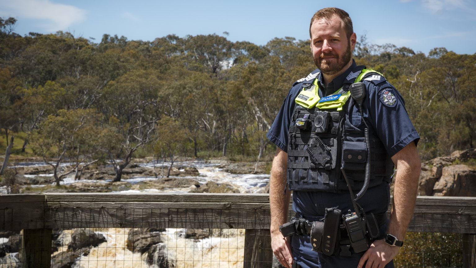 Police Life - image of male member standing in front of a waterfall looking at the camera.