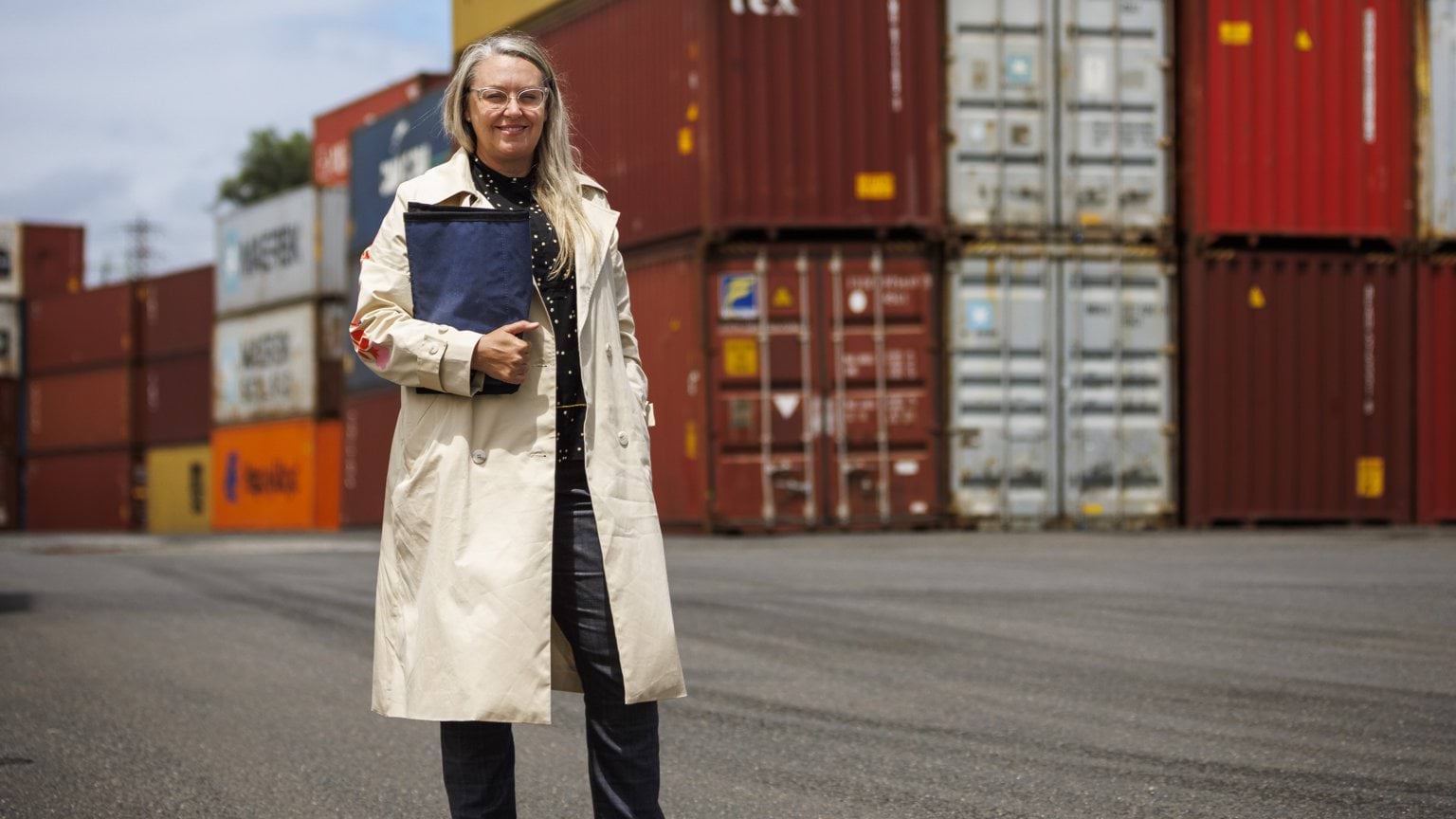 Police Life - Image of female detective in plain clothes standing in front of several shipping containers.