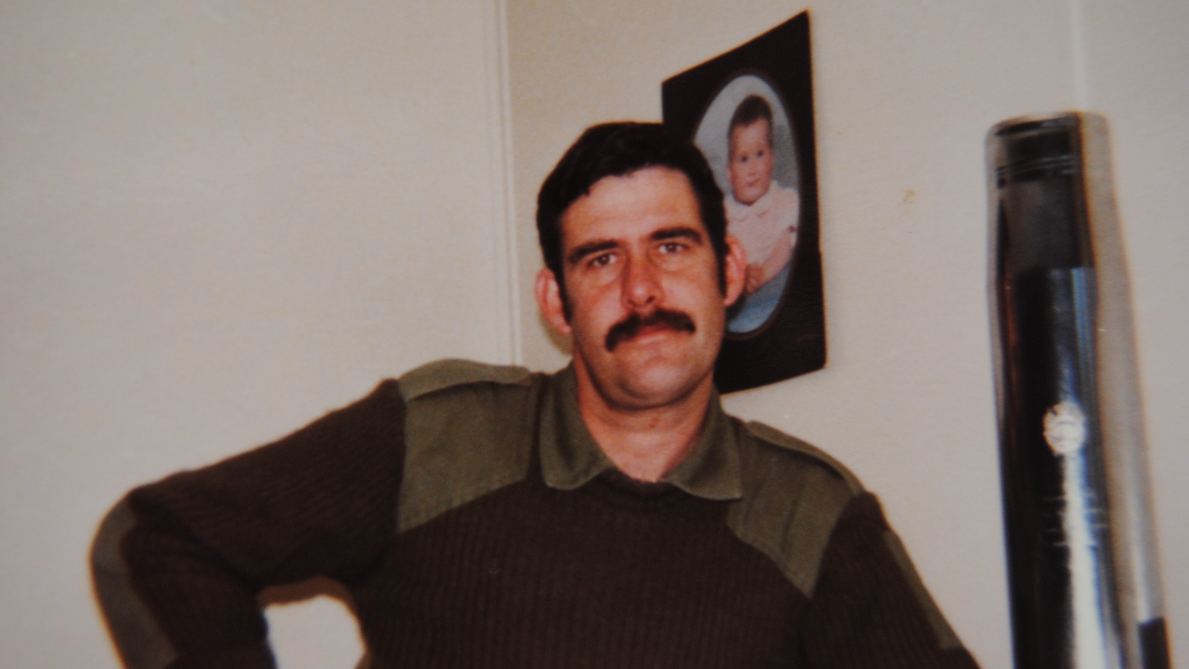 Police Life - Image of man with dark hair and moustache looking at camera.