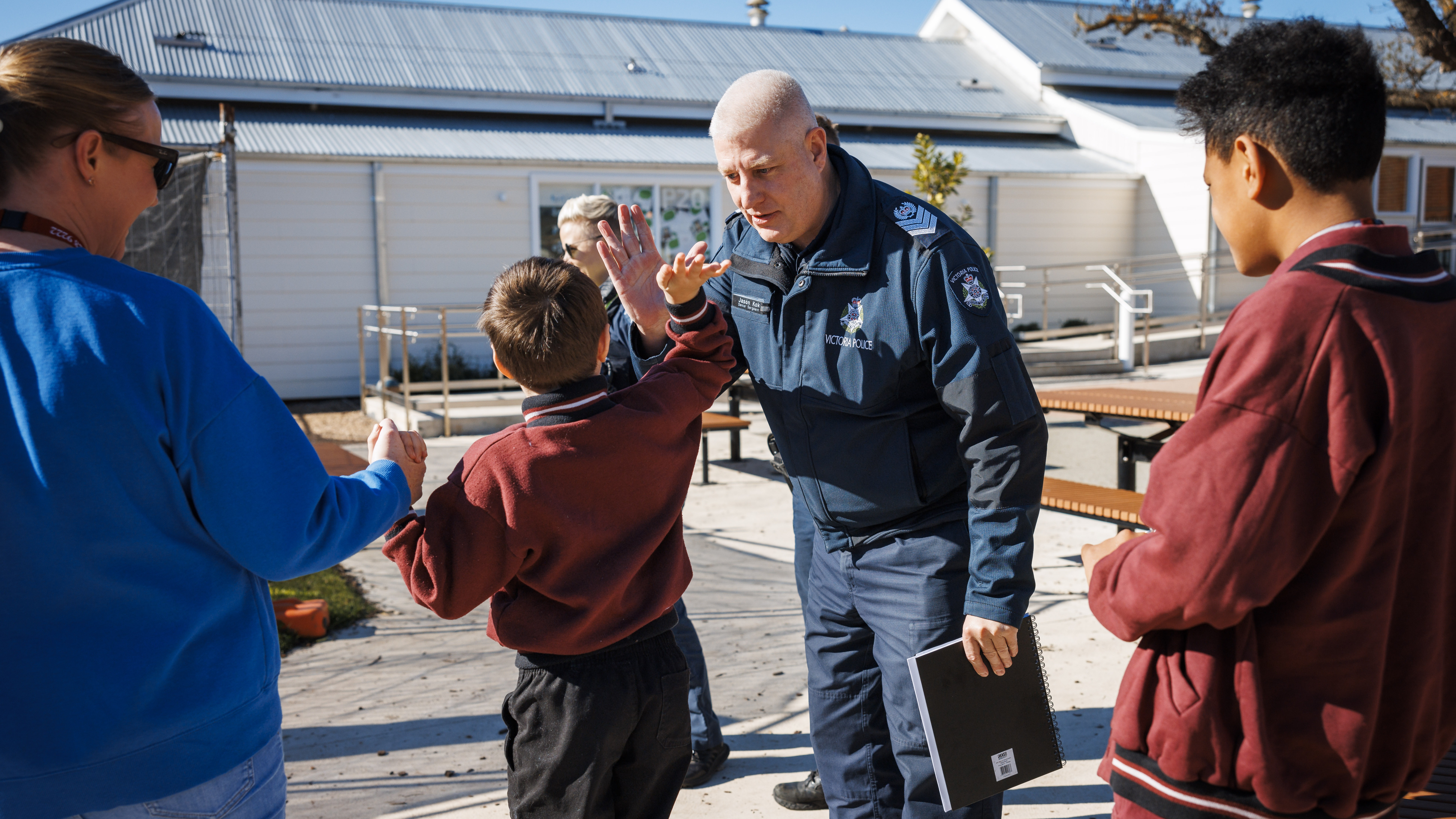 Police Life - Male police Disability Liaison Officer high fives young male student as female staff member and another male student watches