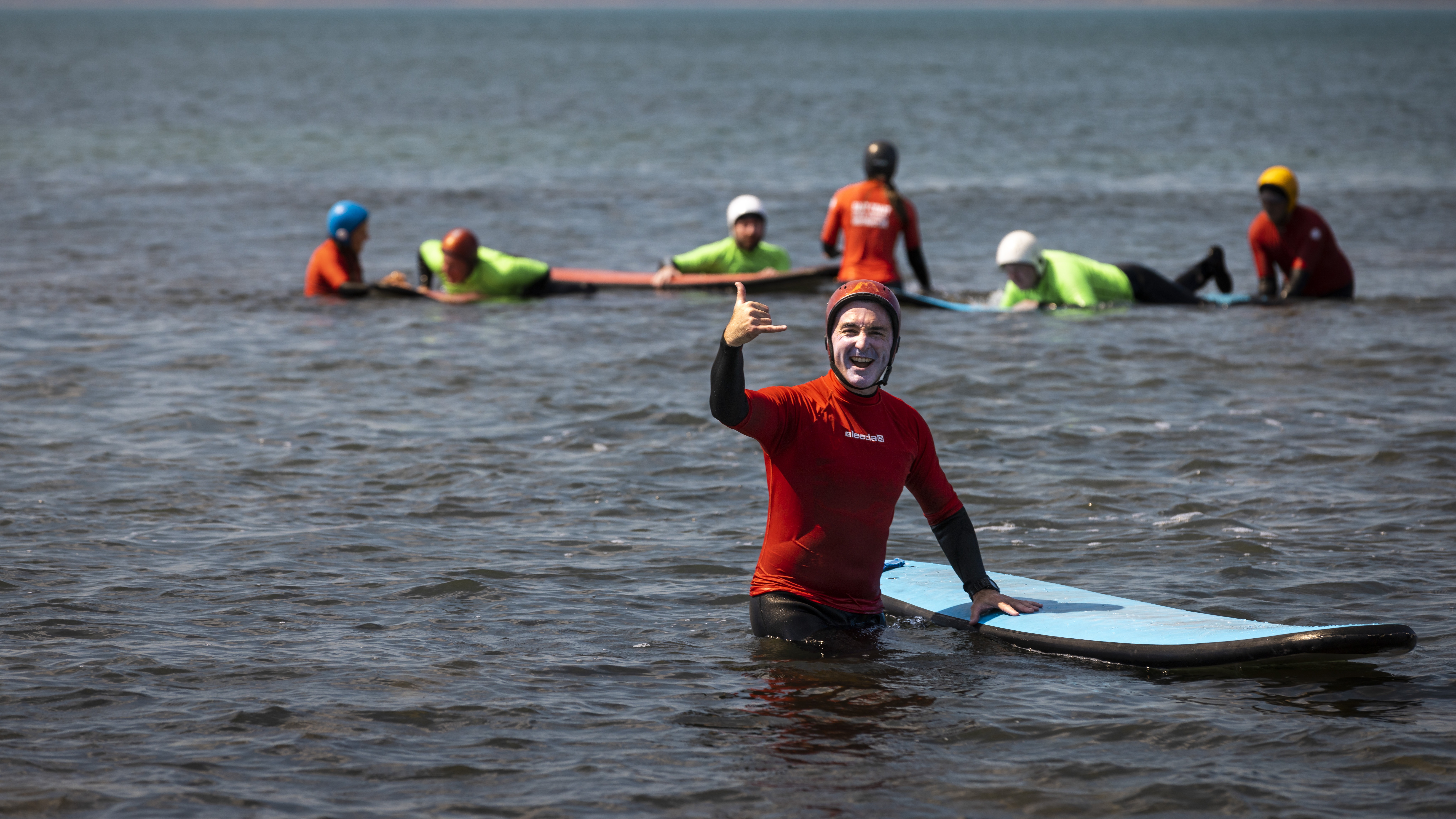 Police Life - A male police officer wearing a red wetsuit standing in the ocean with his surfboard