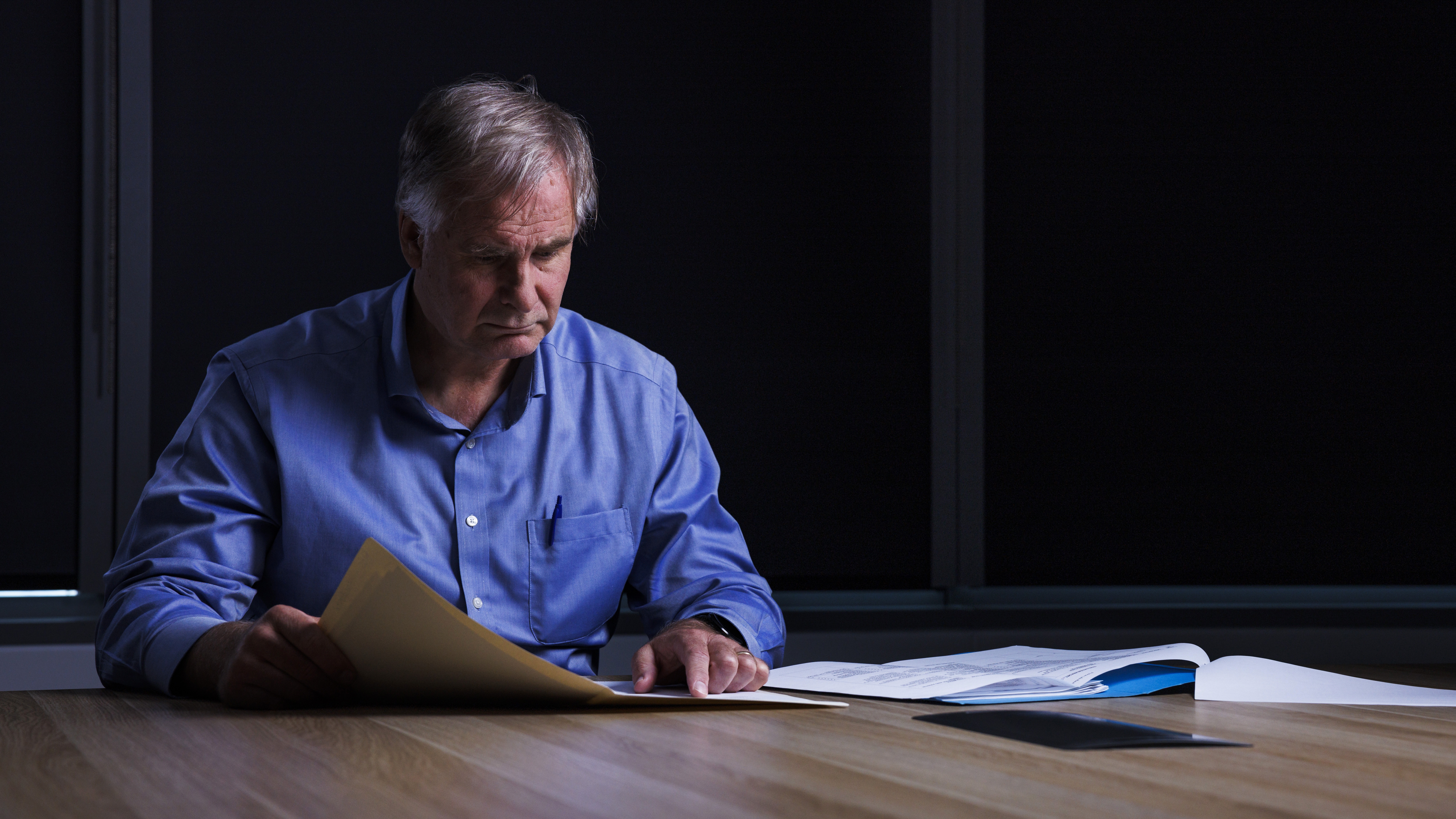 Police Life - Male forensic officer seated at a desk reading documents in a dark room