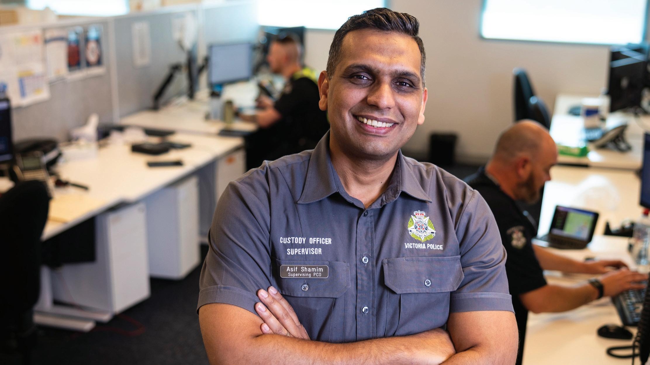Police Life - Male police custody officer standing in a police station office with his arms crossed