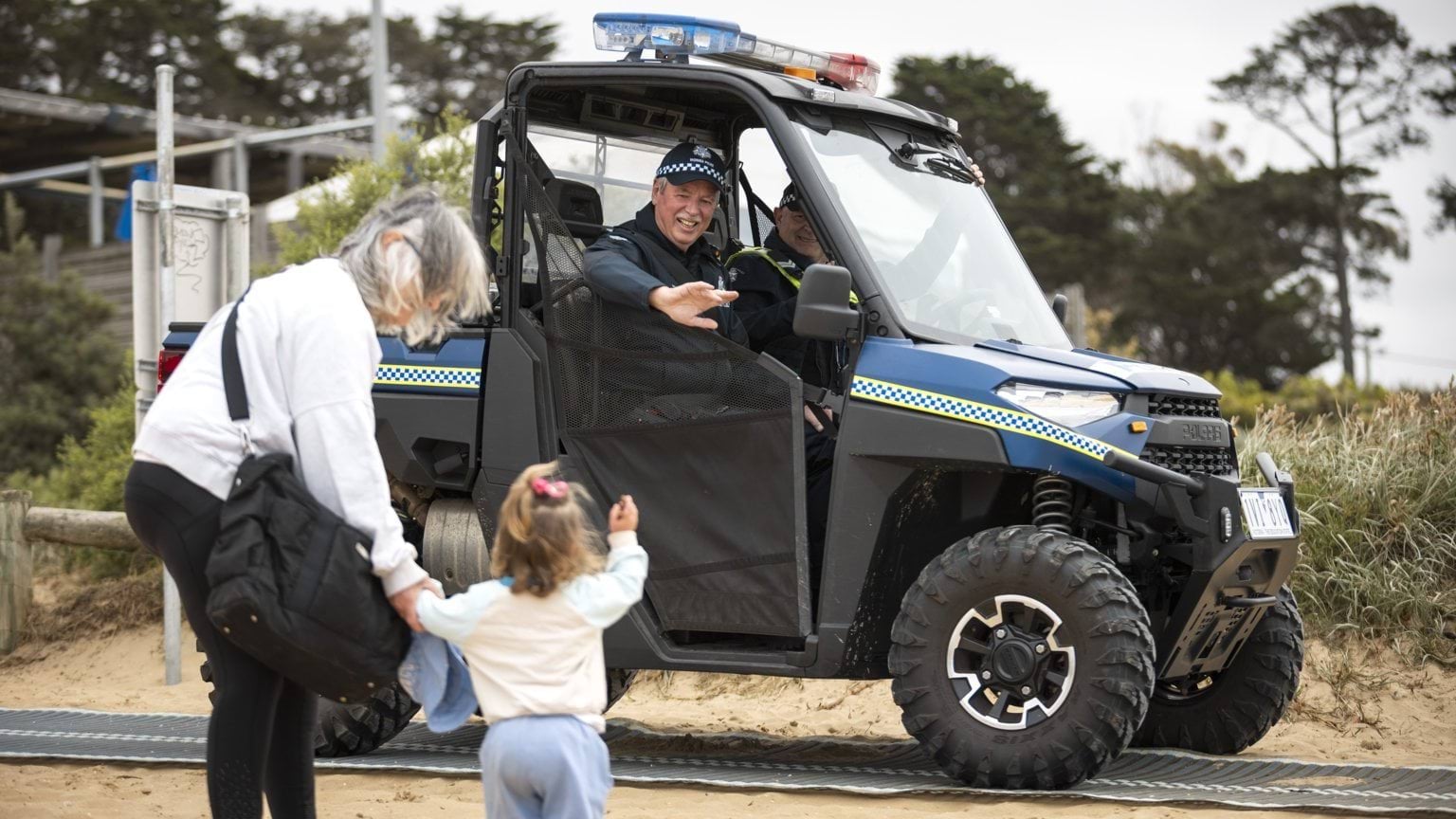 Police in beach buggy wave to people on the beach as they drive past.