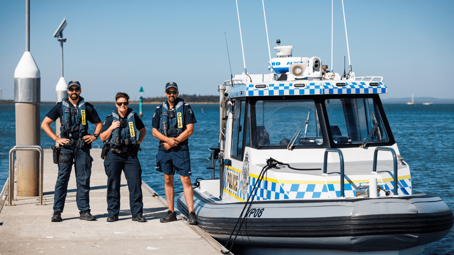 Three police officers wearing life vests stand on a dock next to a police boat