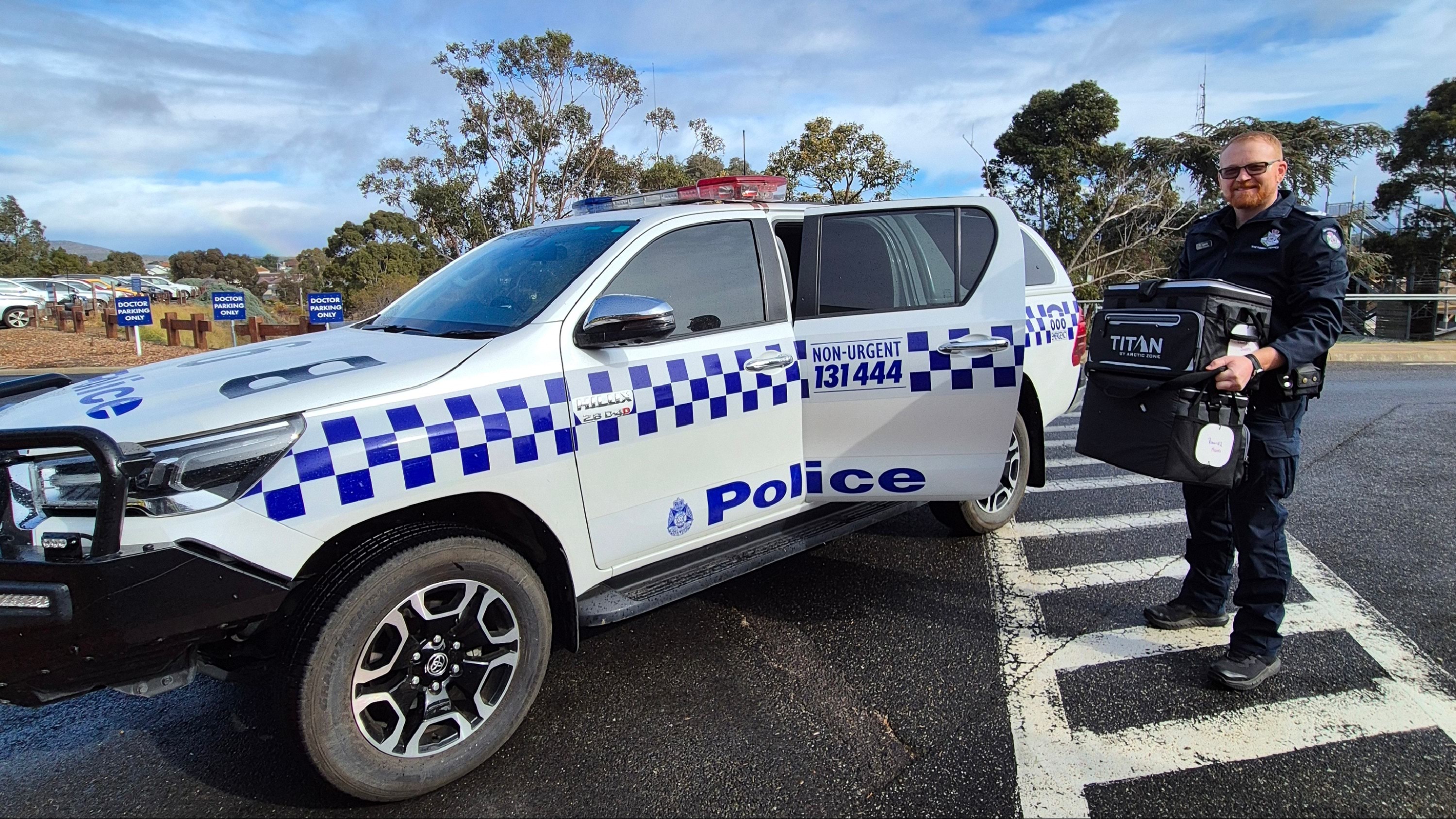 Police member standing in front of a police vehicle with a cooler bag