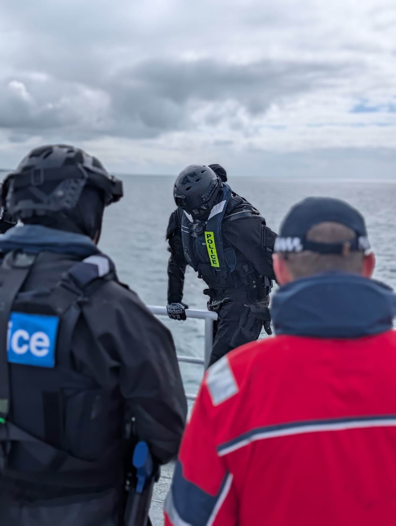 Police members watch on as Acting Sgt Sloane climbs over rails aboard the ferry
