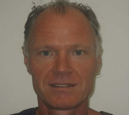 Brendan looking at the camera, with grey-blue eyes, thin grey/black hair and one hoop earring on his right ear. 