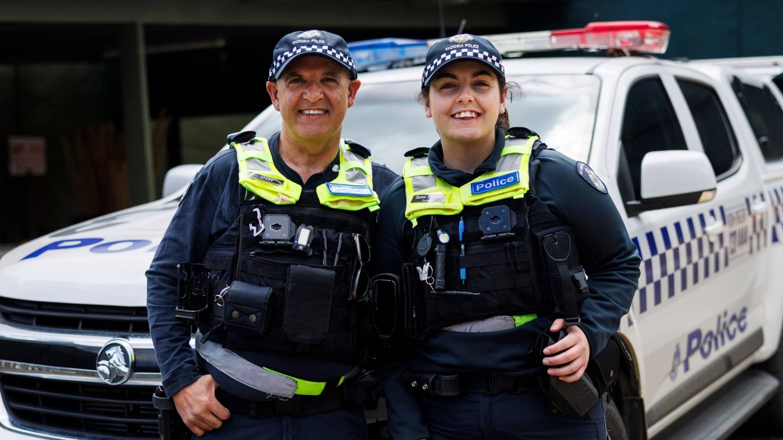 Father and daughter police officer duo standing in front of a police car