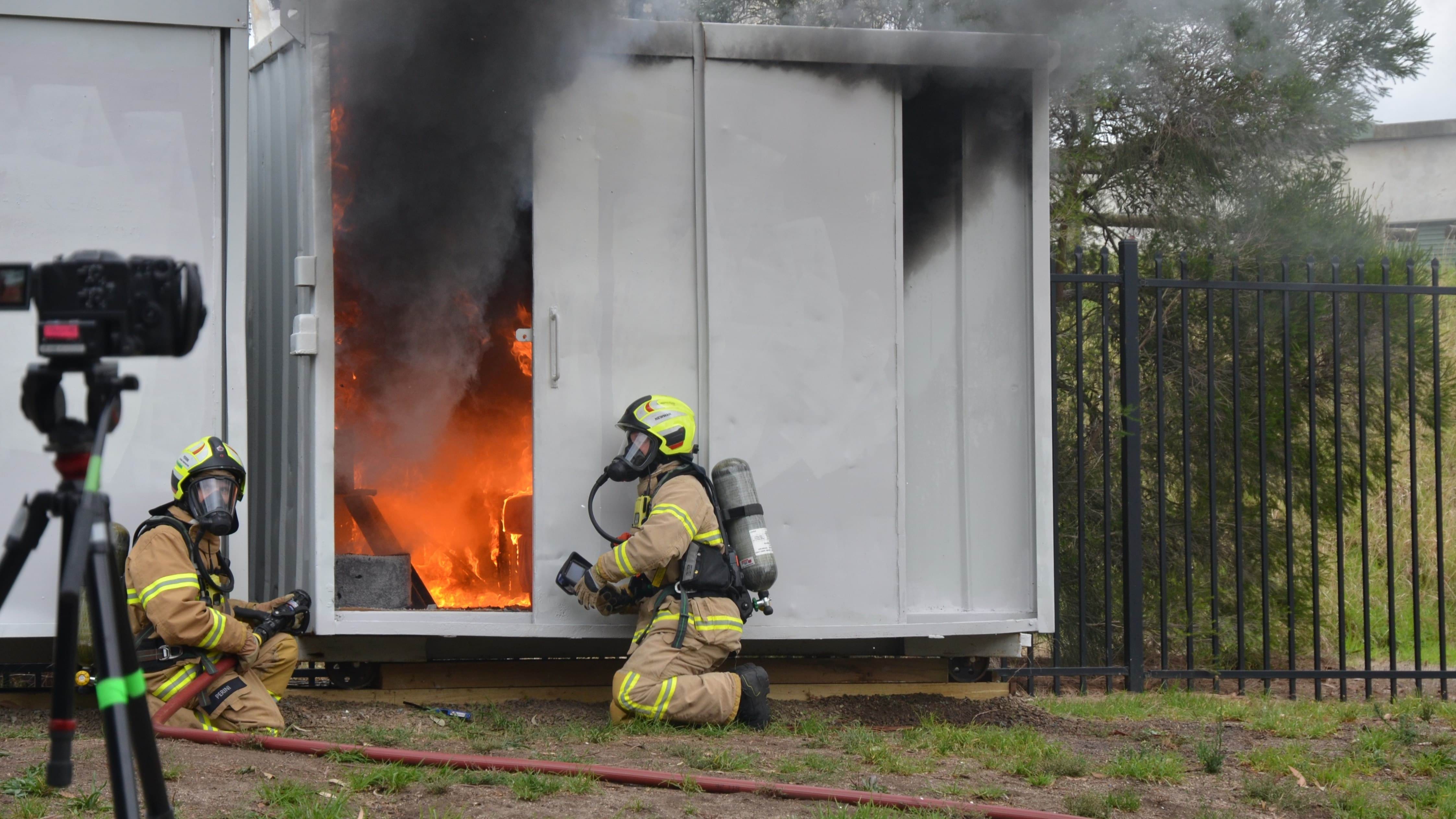 Two Fire Rescue Victoria members crouching next to fire inside shipping container