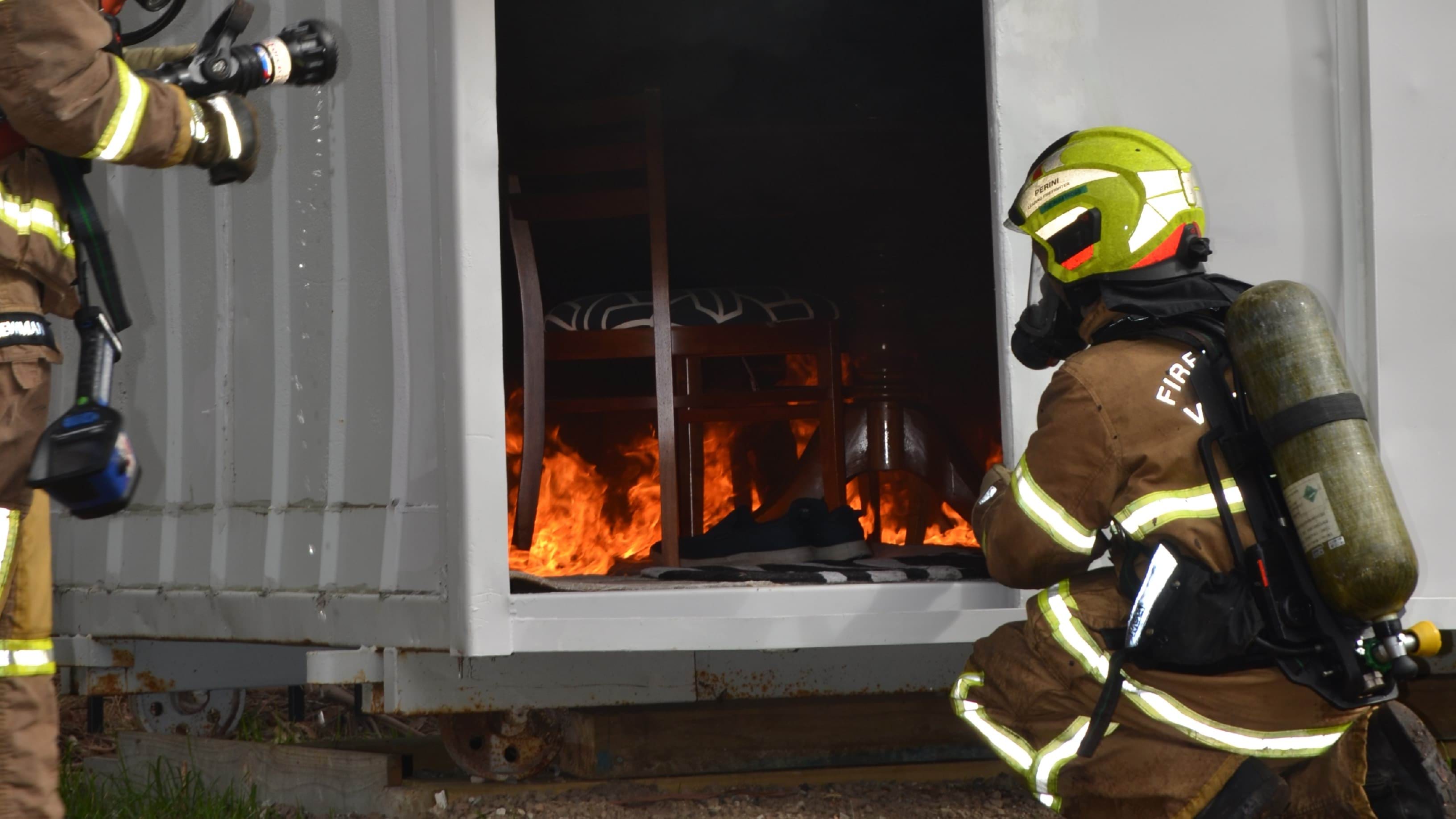 Fire Rescue Victoria member crouching next to fire inside a shipping container