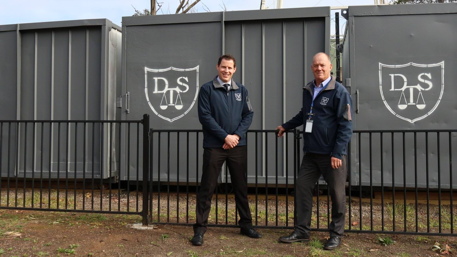 Two members standing in front of grey shipping containers