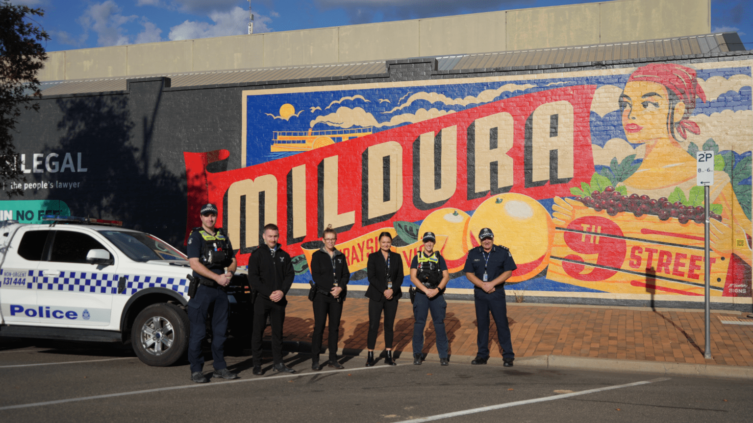 Six Victoria Police members stand in front of a colourful Mildura sign painted on a brick wall.