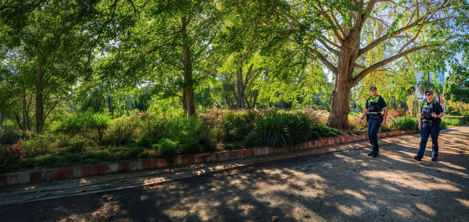 Two police officers walking outside under bright green trees. 