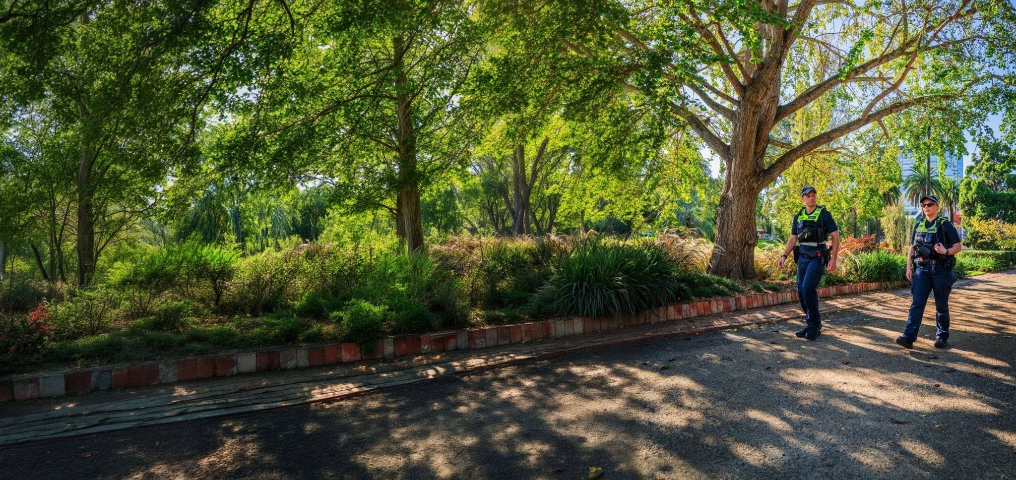 Two police officers walking outside under bright green trees. 