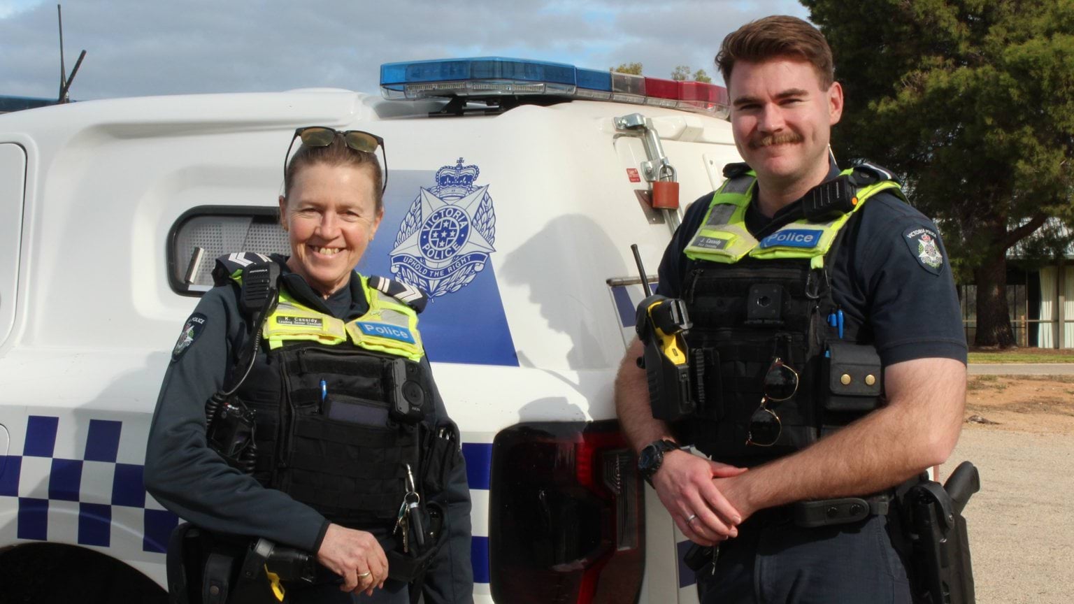 Two members standing in front of a police vehicle