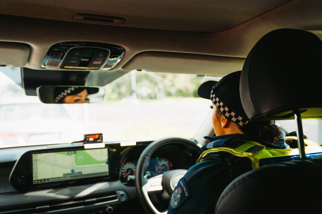 Female Victoria Police officer behind the wheel of a police car, facing ahead, with her eyes reflected in the rear view mirror. 
