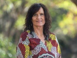 Sue Hine, wearing a red, white and yellow shirt, with long brown wavy hair. 